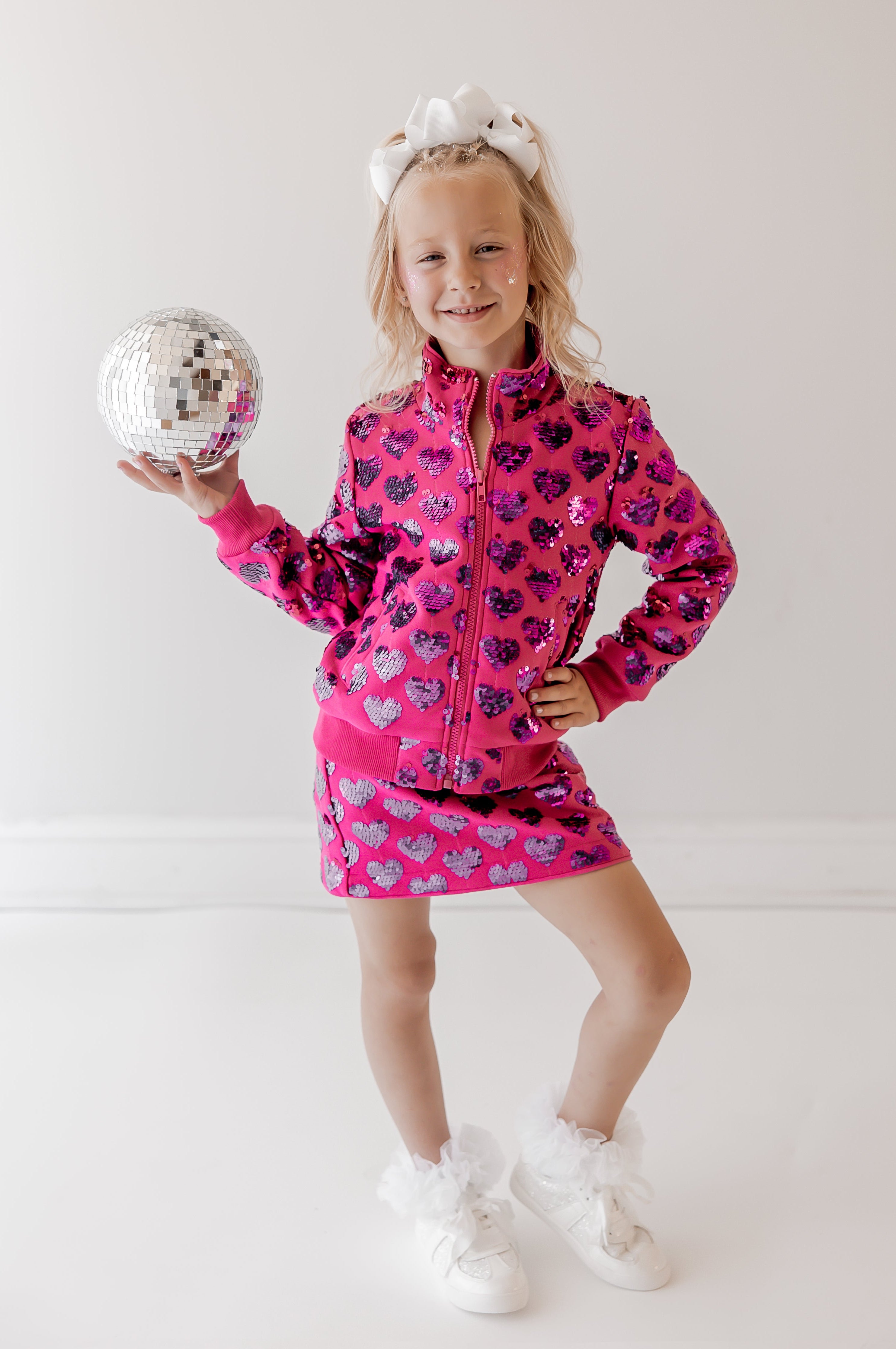 Child wearing a pink outfit with a heart pattern, holding a disco ball on a white background